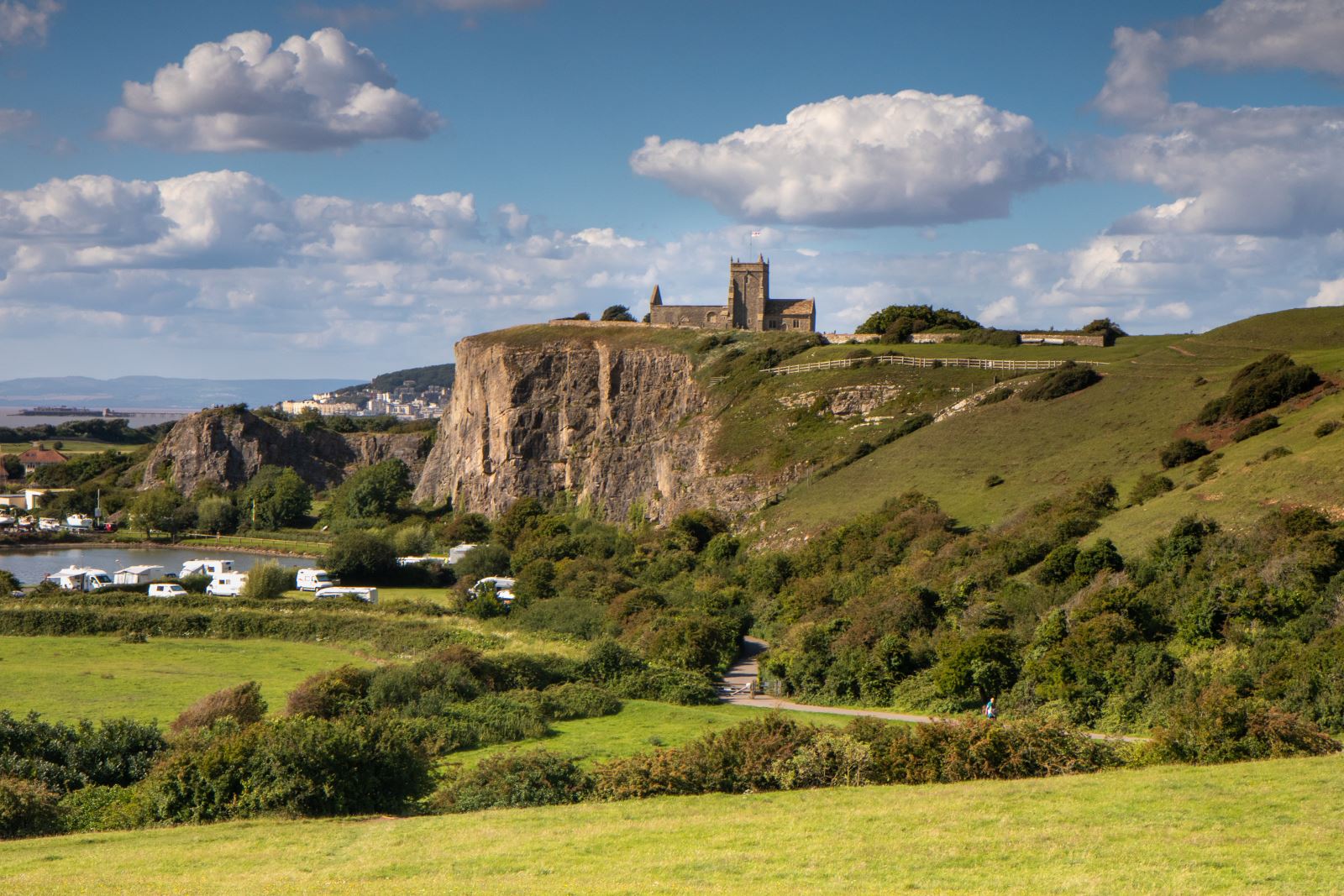 Looking over green fields to the cliff at Uphill, Weston-super-Mare where a church sits atop of a cliff